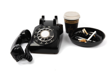 a back rotary telephone, a cup of coffee and an ashtray full of cigarette butts isolated on white
