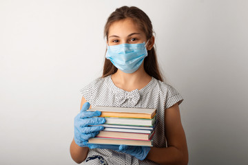 Positive school girl having distance learning. Smiling girl in medical mask and gloves with books