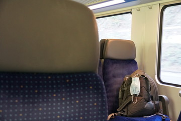 a rucksack on a seat in a train compartment with a N95 facial mask, nose and mouth protection mask, a measure in coronavirus, COVID-19 time, social distancing and infection prevention.