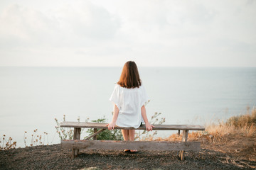 girl in white sitting on a bench watching the sea at sunrise