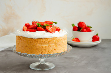 Angel food cake with whipped cream and slices of fresh strawberries on top on a concrete background. Summer dessert. Horizontal orientation, copy space.