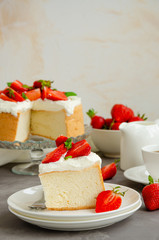 Angel food cake with whipped cream and slices of fresh strawberries on top on a concrete background. Summer dessert. Vertical orientation, copy space.