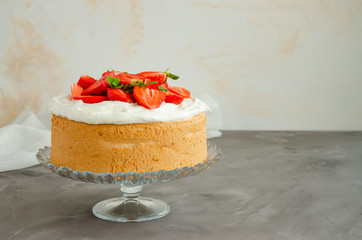 Angel food cake with whipped cream and slices of fresh strawberries on top on a concrete background. Summer dessert. Horizontal orientation, copy space.