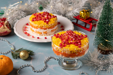 Fototapeta na wymiar Festive New Year's salad with chicken, eggs, carrots and corn, decorated with a star of pomegranate seeds on light blue background, Closeup