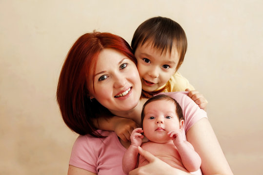 Happy young mother with two children, boy and girl. Portrait of happy mixed race family: smiling mom holding infant baby daughter, elder toddler son is embracing them from behind