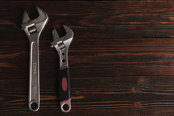 .Shiny wrenches on a brown, rough, wooden background. Chrome adjustable spanners, top view