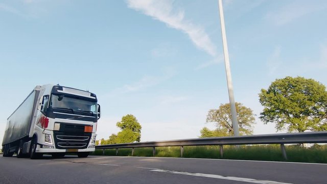 Cargo truck with cargo trailer driving on a highway. White Truck delivers goods in early hours of the Morning - very low angle drive thru close up shot.