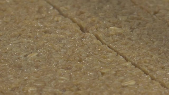 Close up of flapjack or granola cake mix getting sliced by an automated cutter on a conveyor system