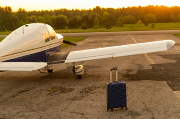 A blue suitcase and a parked small private jet. Quadruple plane with a propeller for an air taxi in the sunset. Self travel concept. plane for VIP persons. © Михаил Решетников