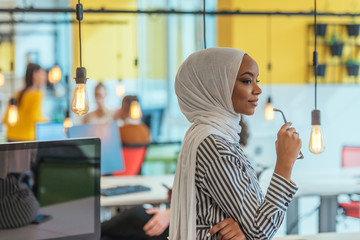 Protrait of a black ( african-american) female muslim standing in a modern business office while...