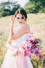 Fototapeta na wymiar Bride in a luxurious white and pink wedding dress in nature at sunset