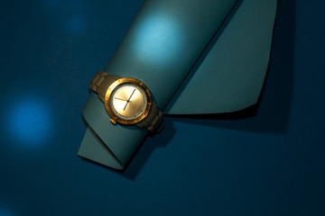 Wristwatch with silicone strap and gold clock face on blue background. Stylish and modern, unisex.