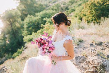 Bride in a luxurious white and pink wedding dress in nature at sunset