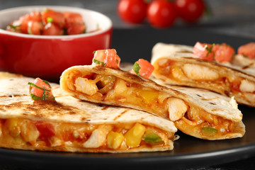 Grilled quesadilla, close-up, with chicken, cheese and vegetables. Served on a black plate with fresh tomato and greens sauce.