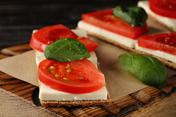 Crispbread with feta cheese, red tomatoes and mini spinach leaves, on a wooden board, closeup