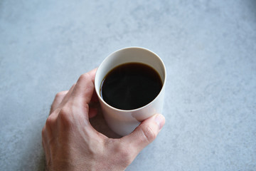 Cup of black coffee in a handmade white ceramics mug, white marble background. Man hands shown.