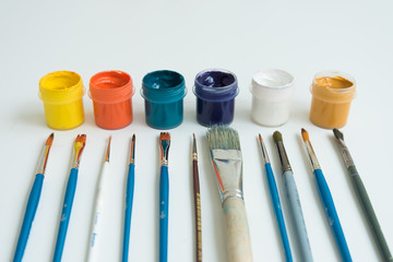 Jars of gouache paint in different colors. Next to it are brushes of various sizes. Artist's kit....