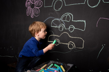 Little boy draws with chalk on a black slate wall. Children's colorful drawings. drawing lessons. the child shows his drawing on the wall. European appearance. close-up.