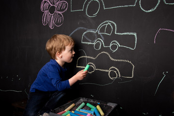 Little boy draws with chalk on a black slate wall. Children's colorful drawings. drawing lessons....