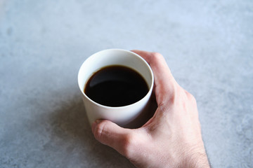 Cup of black coffee in a handmade white ceramics mug, white marble background. Man hands shown.
