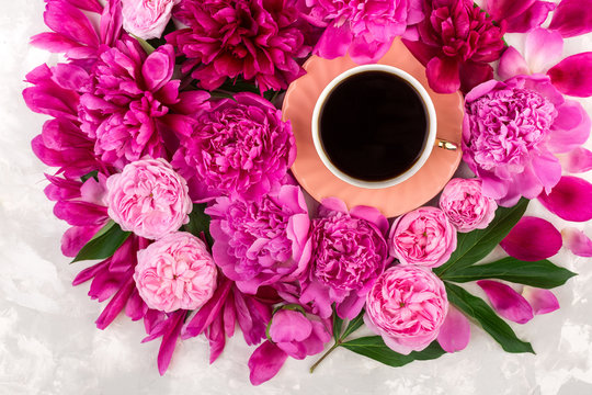 A cup of black coffee surrounded by pink peonies and english roses. Flat lay, top view mock up.
