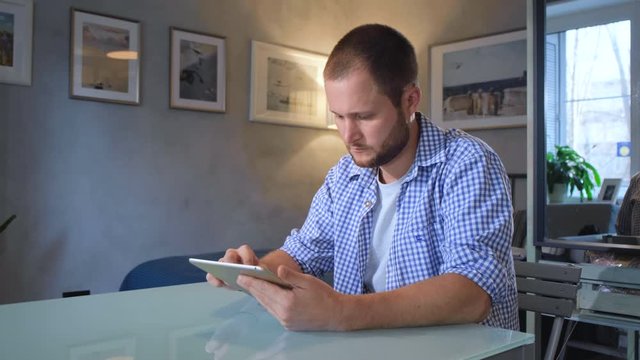 Modern Decorated Home Interior On The Background, Professional Photo And Video Shooting, Close-up. Stock Footage. Young Man Sitting In Comfortable Armchair And Looking At Digital Tablet