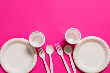 two sets of disposable spoons, forks, plates and glasses of corn starch on a pink background....