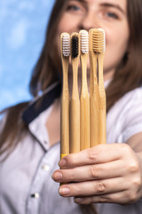 a lot of bamboo toothbrushes in female hands close-up. girl with a defocused smile. environmentally friendly biodegradable hygiene items. multi-colored bristles. place for text