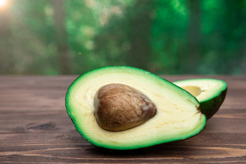 avocado cut in half with a bone on a wooden table against a green bokeh background. healthy food. proper nutrition.