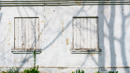 White wooden wall with closed windows with cracks and texture of old paint. Background for your design. Space for text.