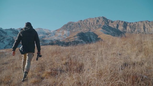 A man in a jacket walks through the mountains. Dried grass, Slow motion, Sunset. Shooting from behind.