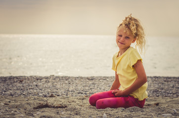 Fototapeta na wymiar sad child sitting alone in sandy beach near the sea