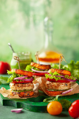 Delicious roasted pumpkin turkey burger with tomatoes and pesto on green wooden board.