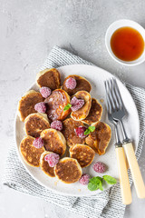 Mini pancakes with raspberries, mint and jam for breakfast on a ceramic plate. Pancakes cooked in the morning for breakfast in the home kitchen.