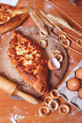 Top view of a delicious traditional Ajarian khachapuri-an open baked pie with melted salted Suluguni cheese and egg yolk on a wooden tray on the table during cooking.