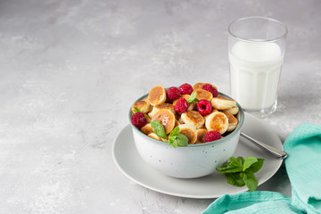Pancakes cereal with raspberries, mint and jam in a ceramic bowl and a glass of milk. Trendy food, tiny funny crumpet, children's food. Breakfast.