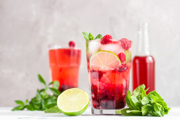 Cold pink non-alcohol cocktail with raspberry, lime, mint and ice cubes on light grey concrete background.