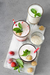 Layered strawberry and raspberry smoothie or milkshake in glasses decorated with mint, raspberry and coconut flakes on grey table. Healthy food for breakfast or snack.