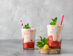 Strawberry and raspberry smoothies in glasses garnish with mint and raspberry on wooden cutting board.