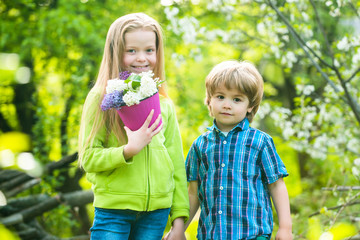 Two little children holding flowers in pot together for prepare plant on ground. Save world concept.