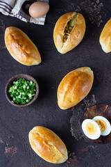 Fresh baked patties with egg and green onion stuffing. Dark brown stone table. Traditional Russian and Ukrainian homemade savory pirozhki. Rustic style.