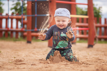 An 11 month old boy throws sand in the air.
