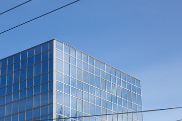 Part of a glass mirrored office building reflecting the blue sky.