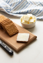 Butter spread on crispy square cookies on a wooden plate