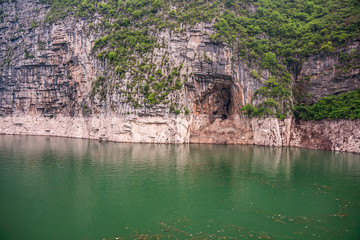 Wushan, Hubei, China - May 7, 2010: Wu Gorge in Yangtze River. Cave hole barely above green water in brown-gray rocky cliff with some green foliage.