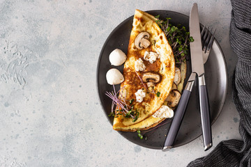 Homemade omelette with mushroom, mozzarella and microgreens on plate over light concrete...
