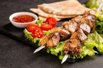 Two portions of shish kebab on a stone plate with salad.