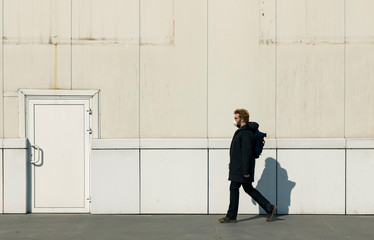 Fototapeta na wymiar man in mask walking alone profile portrait in black coat cloth, industrial background wall and door