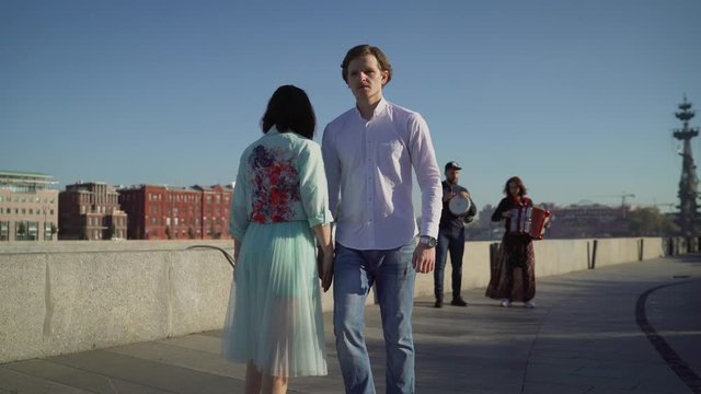 A young couple dancing to live music on the street. Musicians play, and a young couple dancing on the promenade. Music street performers couple with girl violinist and man guitarist on blue sky