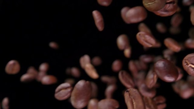 Close-up view of roasted coffee beans flying diagonally on the black background in slow motion